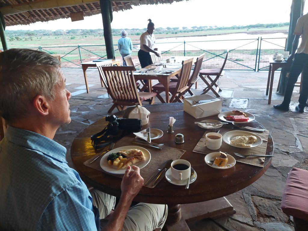 Chet sitting at the breakfast table of the Voi Wildlife Lodge, enjoying the scenic savanna.